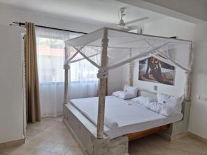 a bedroom with a canopy bed with white sheets and pillows at Nyumba Maua B&B in Watamu