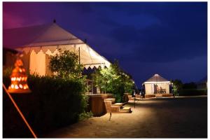 Tienda blanca con mesa y sillas por la noche en Barna desert camp jaisalmer, en Kūri