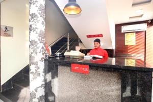 a man in a red shirt sitting at a counter at Hotel O B1 in Kartārpur