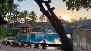 een vrouw zittend op stoelen bij een zwembad in een resort bij The Jayakarta Residence 2BR Bali in Denpasar