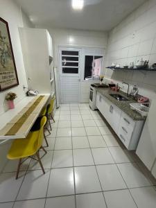 a white kitchen with a counter and yellow chairs in it at Casa Sol & Churrasco in Guarujá
