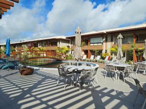 un patio con mesas y sombrillas junto a una piscina en Condominio con Piscina a 450m de la Playa en Itacimirim - VBRs, en Pojuquinhos