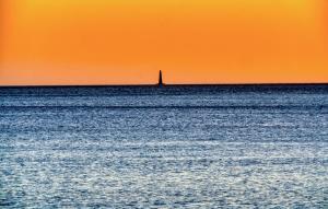 Ein Boot auf dem Meer, in der Ferne ein Leuchtturm. in der Unterkunft Charmant Appartement in Saint-Georges-de-Didonne