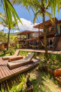 a house with a wooden deck with chairs and palm trees at Pousada Canto Bravo in Ilhabela