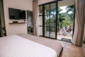 Un dormitorio con una cama y un hombre sentado en un balcón en KAI BAE BALCONY Hills Bungalows Koh Chang, en Khlaung Phai Bae