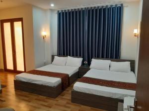 two beds in a hotel room with blue curtains at Nhà nghỉ 79 Ocean Park 2 in Ðình Loan
