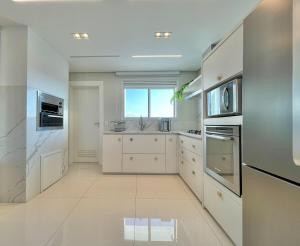 a kitchen with white cabinets and a large window at Phoenix Tower FG - Lazer Resort a Passos do Mar BC in Balneário Camboriú