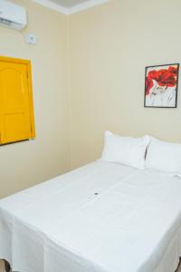 a bedroom with a white bed with a yellow door at Eco Hotel Mãe De Sagui in Castanhal