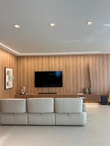 Apt luxo vista mar 160m com jacuzzi e 2 garagens في ايتابيما: غرفة معيشة مع أريكة بيضاء وتلفزيون بشاشة مسطحة