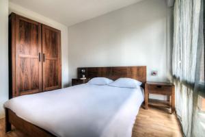 a bedroom with a white bed and a wooden cabinet at Comfort Aparthotel Lourdes L'Acacia in Lourdes