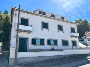 a white building with green shutters on a street at Gouveia Forest Guest House in Gouveia