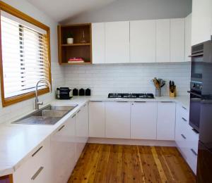 Una cocina con gabinetes blancos y un fregadero. en Lilly Pilly at Callala Beach, en Callala Beach