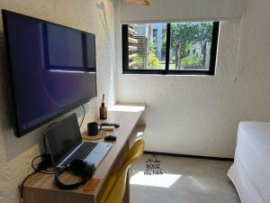 a room with a desk with a laptop and a television at Milagres - VIllas Patacho in Pôrto de Pedras