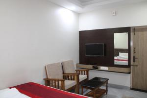 ein Schlafzimmer mit einem Bett und zwei Stühlen und einem Fernseher in der Unterkunft SRG Shivam Residency in Tiruvannāmalai