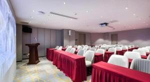 une salle avec des tables rouges et des chaises blanches et un podium dans l'établissement Echarm Hotel Huzhou Wuyue Plaza Children's Clothing City, à Jijiawan