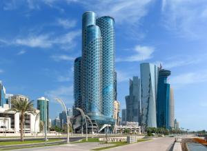 a tall blue building in front of a city at Swissôtel Corniche Park Towers Doha in Doha