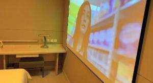 un écran de projection dans une pièce avec un lit et un bureau dans l'établissement Jinjiang Inn Wuhan Huanghelou Fuxing Road Metro Station, à Wuhan