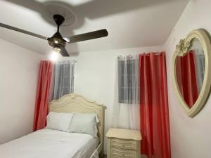 a bedroom with a bed with red curtains and a ceiling fan at 1DR Charming 3-Bedroom Retreat Santo Domingo in Santo Domingo