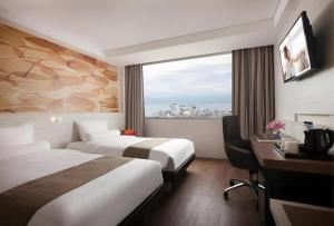 a hotel room with two beds and a desk and a window at Royal Bay Hotel Makassar in Makassar