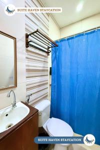 a bathroom with a toilet and a sink and a blue shower curtain at Suite Haven Staycation in Sampong +11 photos