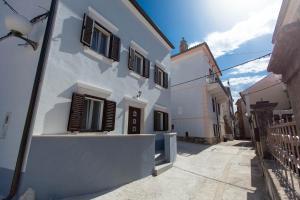 a white building with black shutters on a street at Holiday Home NiKa in Omišalj