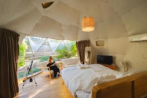une femme assise dans une pièce avec un lit et une fenêtre dans l'établissement The X10 Nordic Tent and Glamping Pool Villa Khaoyai เขาใหญ่ - SHA Certified, à Ban Thung Sawang