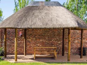 a brick building with a bench and a straw roof at Andela Guesthouse in Bloemfontein +11 photos