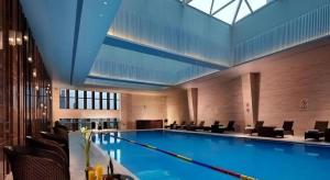 a large swimming pool in a building with chairs at New Century Grand Hotel Hangzhou Shengtai in Hangzhou