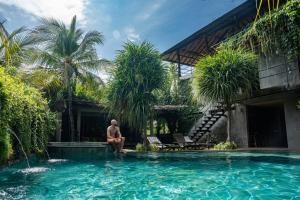 a man sitting in a swimming pool next to a house at Mangroove Bay Boutique Hostel in Banyuwedang