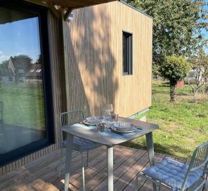 une table et des chaises assises sur une terrasse avec une fenêtre dans l'établissement La Tiny Boisée, à Saulzoir