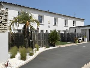 a white house with a fence and a palm tree at Gite La Paillotte, Ile De Ré in Sainte-Marie-de-Ré
