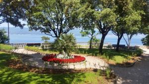 a garden with a fountain with red flowers and trees at Gospoja Park & Beach Apartment Vrbnik in Vrbnik