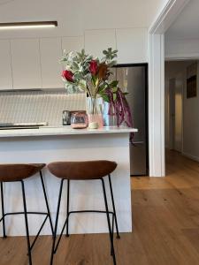 une cuisine avec un comptoir et deux tabourets de bar dans l'établissement PISTE LUXURY CHALET - THE GRANDE - Oaks Lake Crackenback Resort, à Crackenback