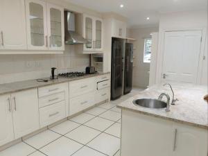 a white kitchen with white cabinets and a sink at Pioneer Guest House in Kloof