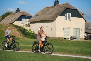 dos personas montando bicicletas delante de una casa en Beachvilla Luxe met Sauna - 6 personen, en Holle Poarte