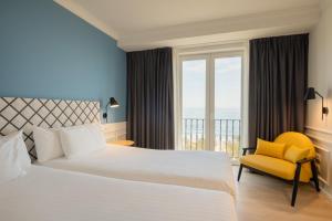 a bedroom with a large bed and a yellow chair at Dorma Sardinero in Santander +34 photos
