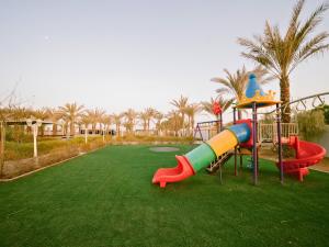 a playground with a slide in a park with palm trees at Palm Escape Farmhouse - By Seven Elements in Ras al Khaimah
