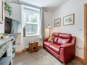a living room with a red leather couch and a flat screen tv at Stanley Cottage in Windermere