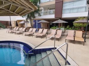 a pool with chairs and umbrellas next to a building at Apartamento Familiar - Casa Da Madeira in Caldas Novas