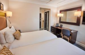 a hotel room with two beds and a desk at Thistle London Heathrow Terminal 5 in Hillingdon
