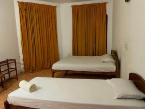 two beds in a room with orange curtains at Mimosha holiday inn in Godapola
