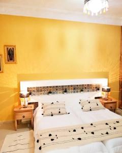 a bedroom with a white bed with a yellow wall at Dar Naifer in Tozeur