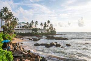 Eine Frau mit einem Sonnenschirm sitzt an einem Strand in der Nähe des Meeres in der Unterkunft Omni Holiday Bungalow in Mount Lavinia