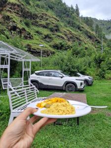 Una persona sosteniendo un plato de comida con un coche al fondo. en Nirvana River Nest, en Sainj
