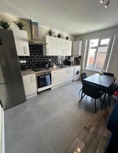 une cuisine avec des armoires blanches et une table avec des chaises dans l'établissement HP Wizards Corner Spacious 4 bed near Watford Junction, à Watford