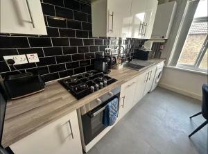 a kitchen with white cabinets and black tiles on the wall at HP Wizards Corner Spacious 4 bed near Watford Junction in Watford