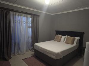 a bedroom with a bed with white sheets and a window at Akwaaba Fie Guesthouse in Lebowakgomo