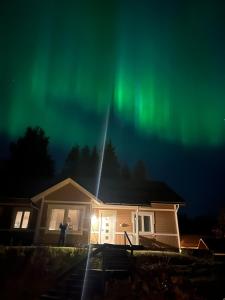 Eine Person steht vor einem Haus unter den Nordlichtern in der Unterkunft House santas in Rovaniemi
