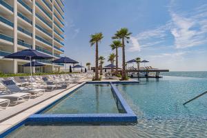 a swimming pool with chairs and umbrellas next to the ocean at Beautiful 2 bedroom condo Encantame Tower E 802 in Puerto Peñasco