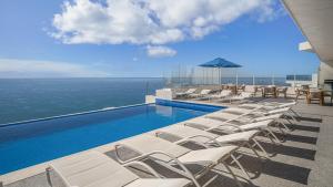 a swimming pool with white lounge chairs and the ocean at Encantame Towers Verano 1401 in Playa Encanto